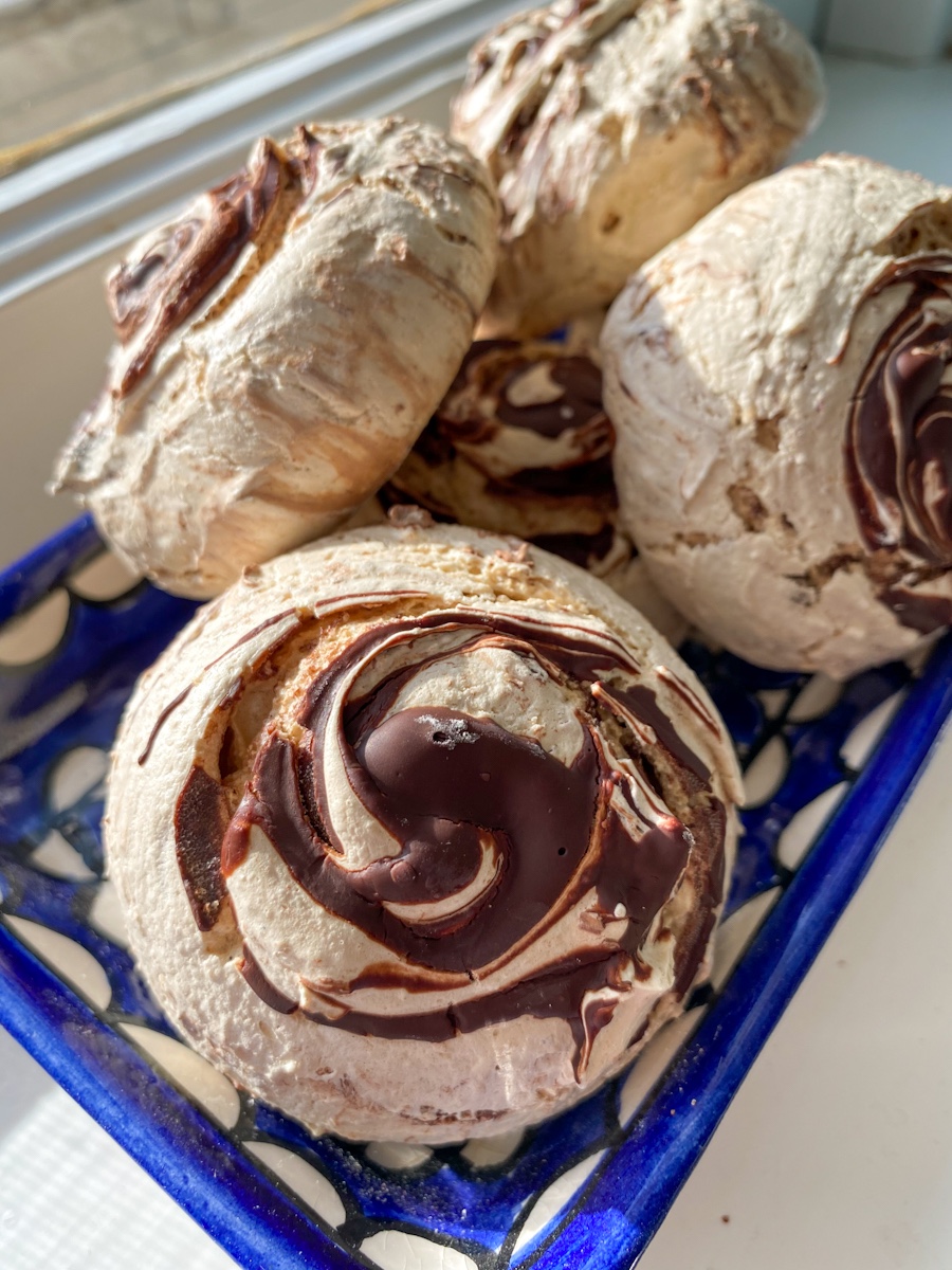 Large round meringues swirled with chocolate sit on a blue and white plate.