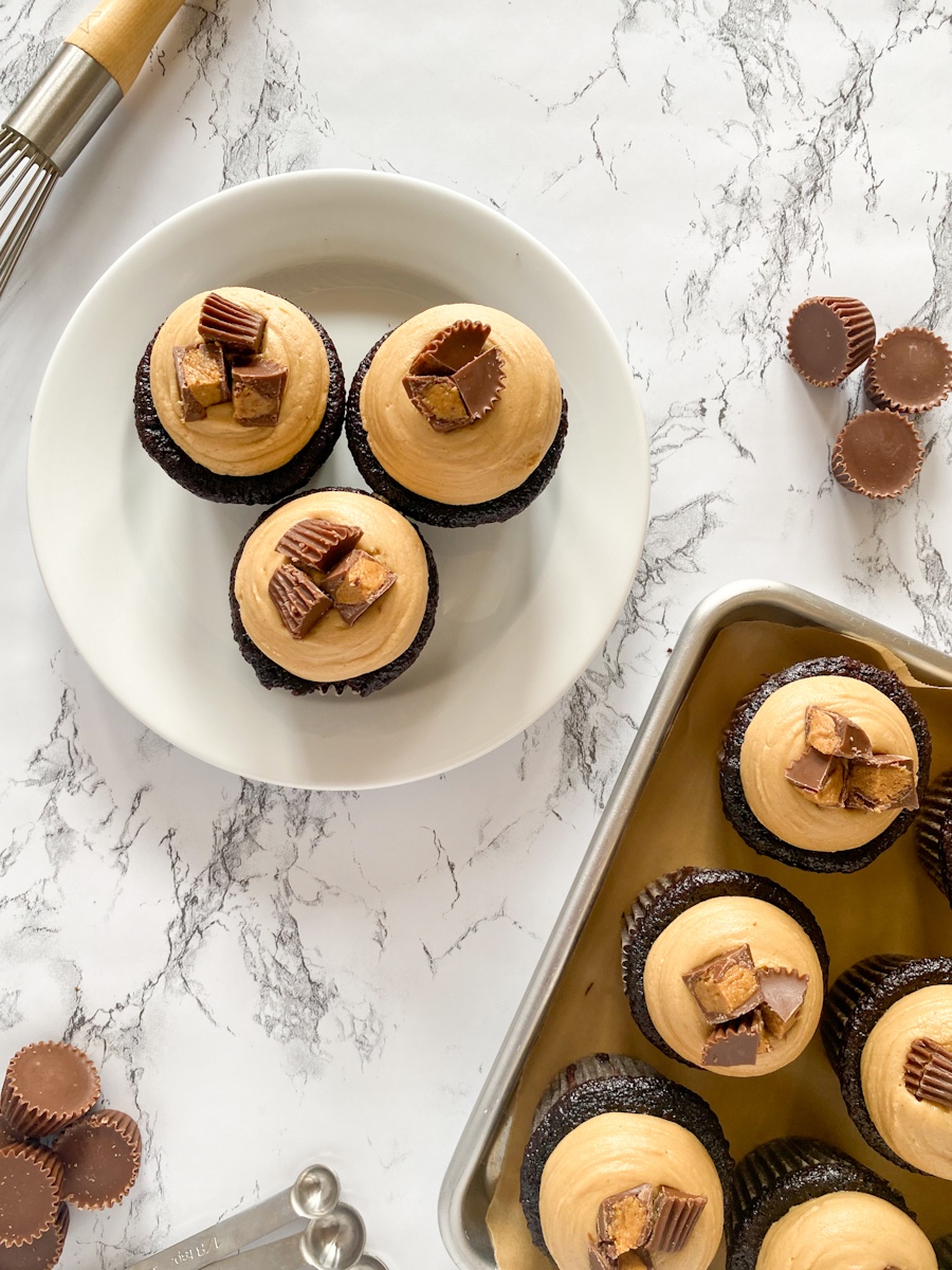 chocolate cupcakes with peanut butter frosting arranged on a white plate on a marble surface.