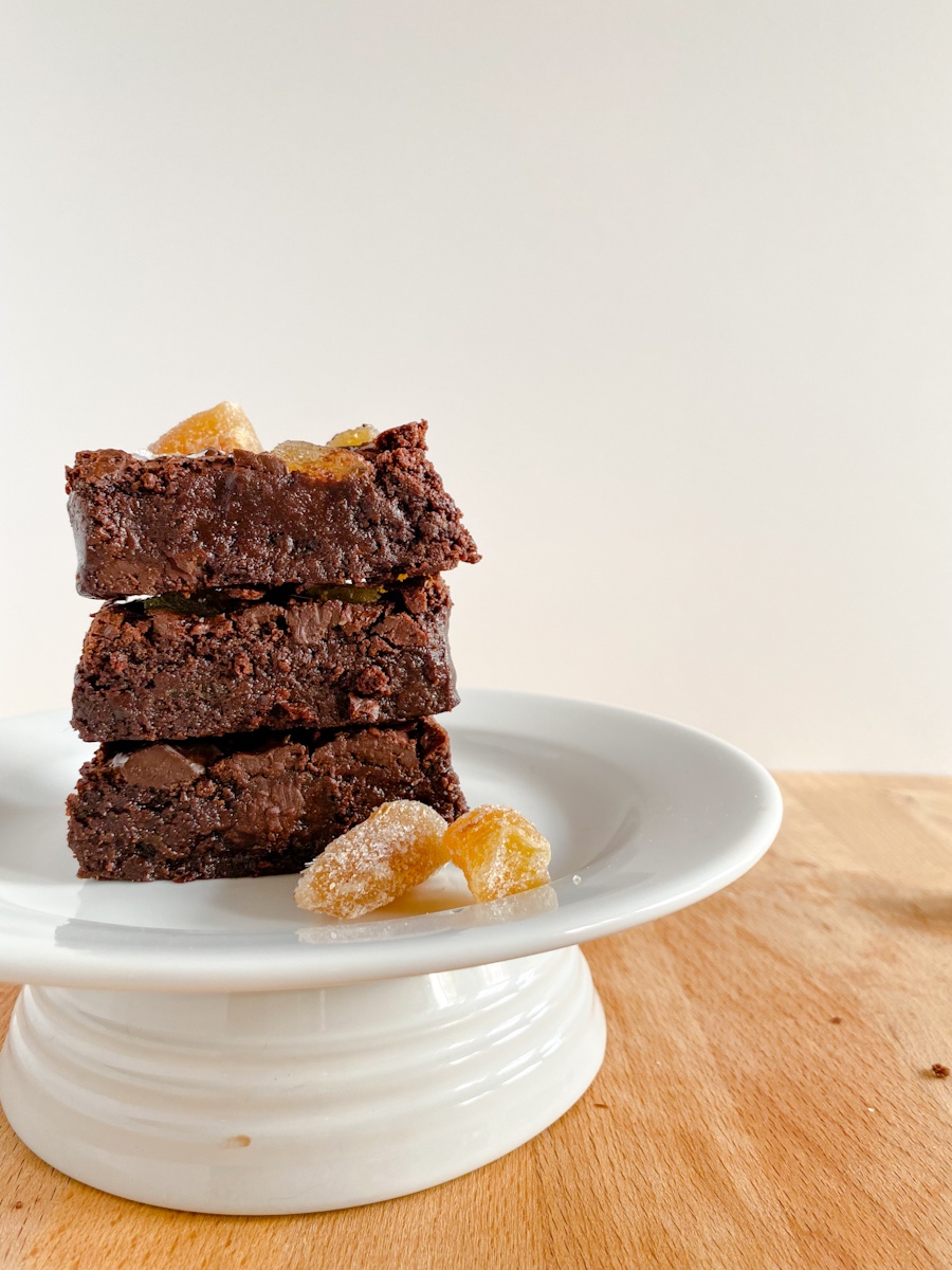 a stack of brownies sit on a raised white plate on a wooden surface with a white background.