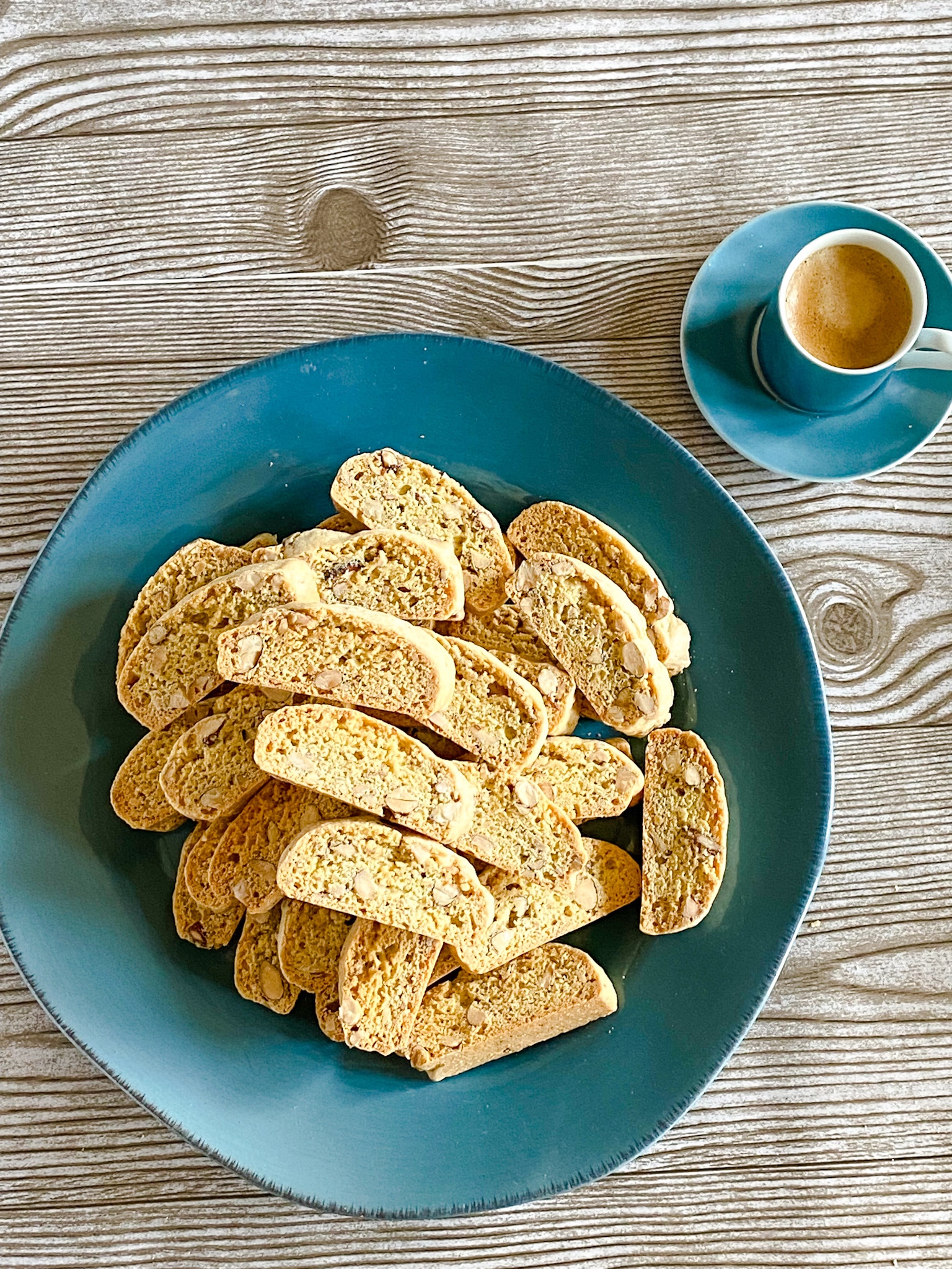 Mini almond biscotti piled on a blue plate on a woodgrain surface.