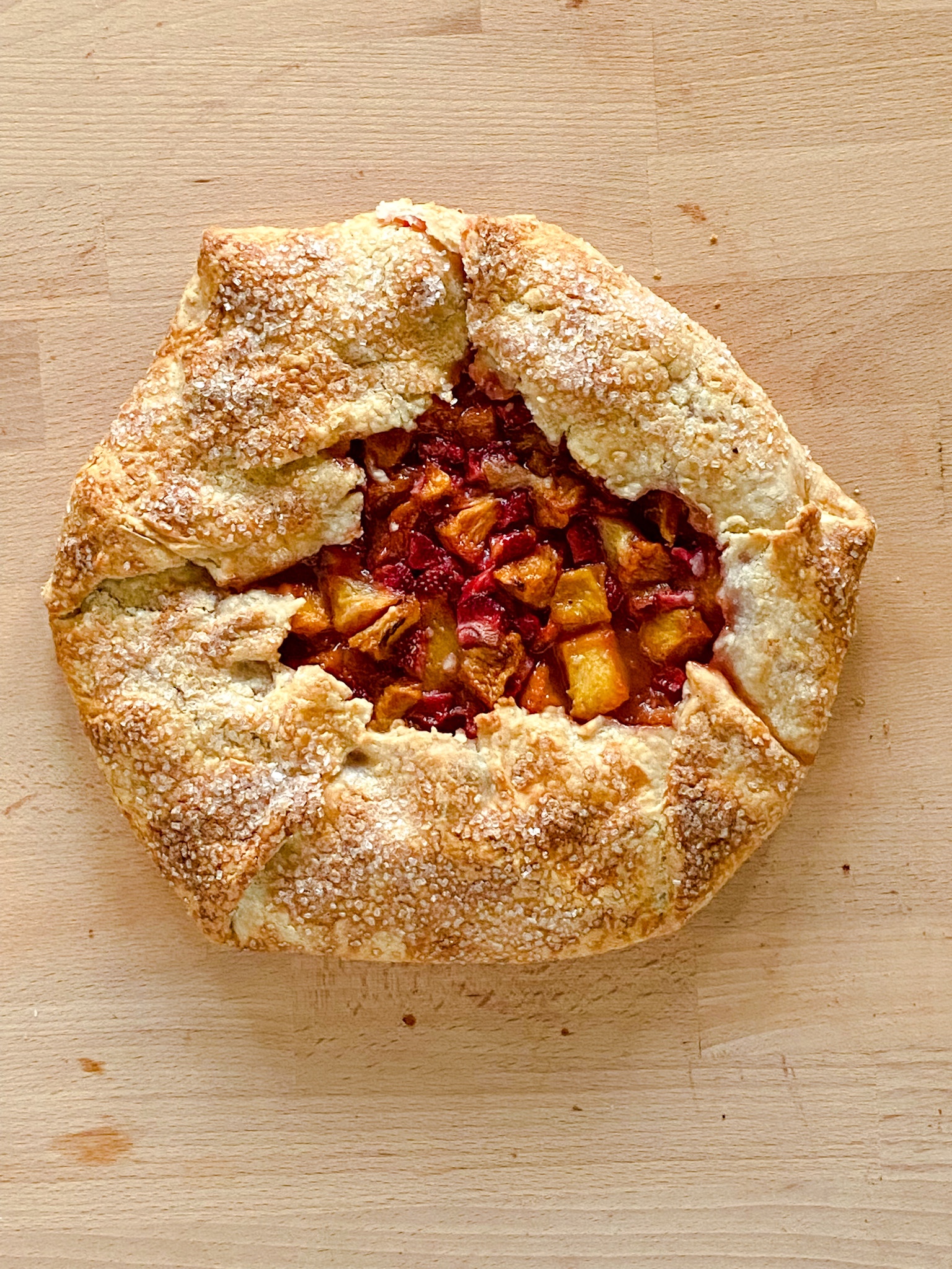 A single crust rustic tart filled with red and yellow fruits sits on a wooden surface.