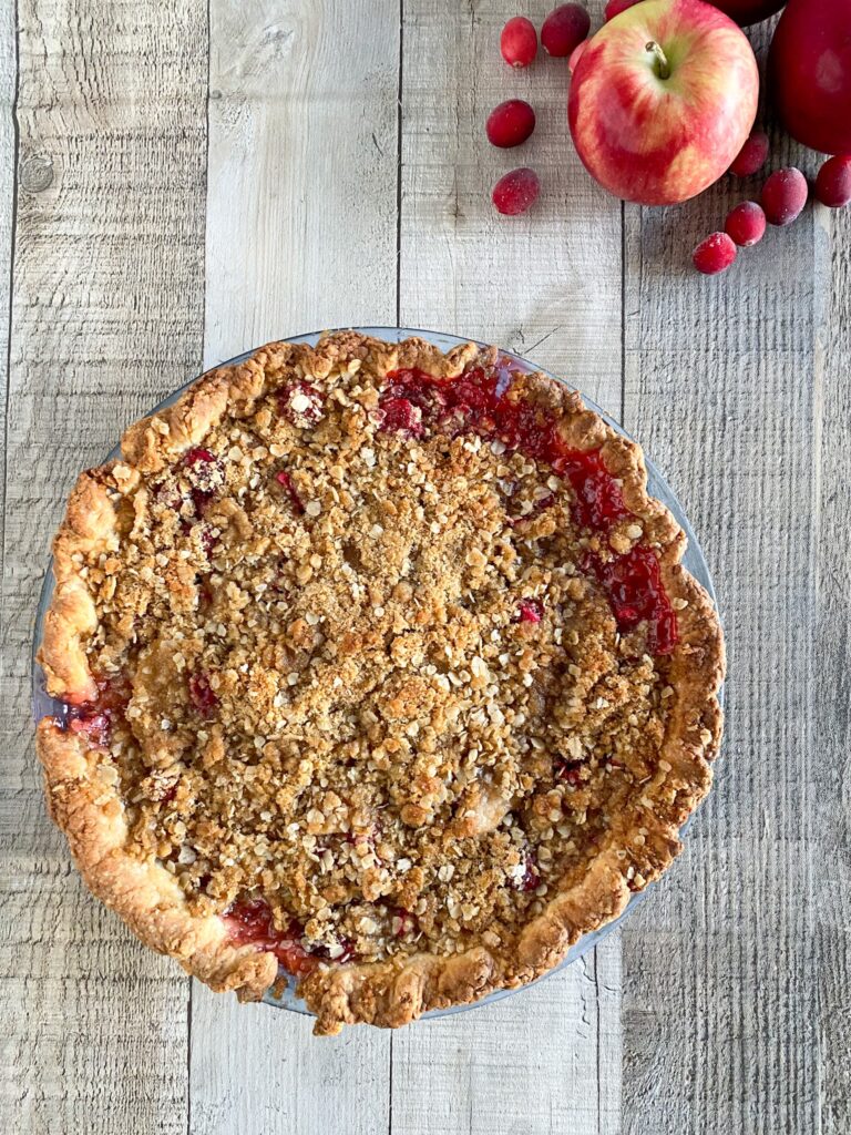 A crumble-topped cranberry apple pie sits on a wooden surface.