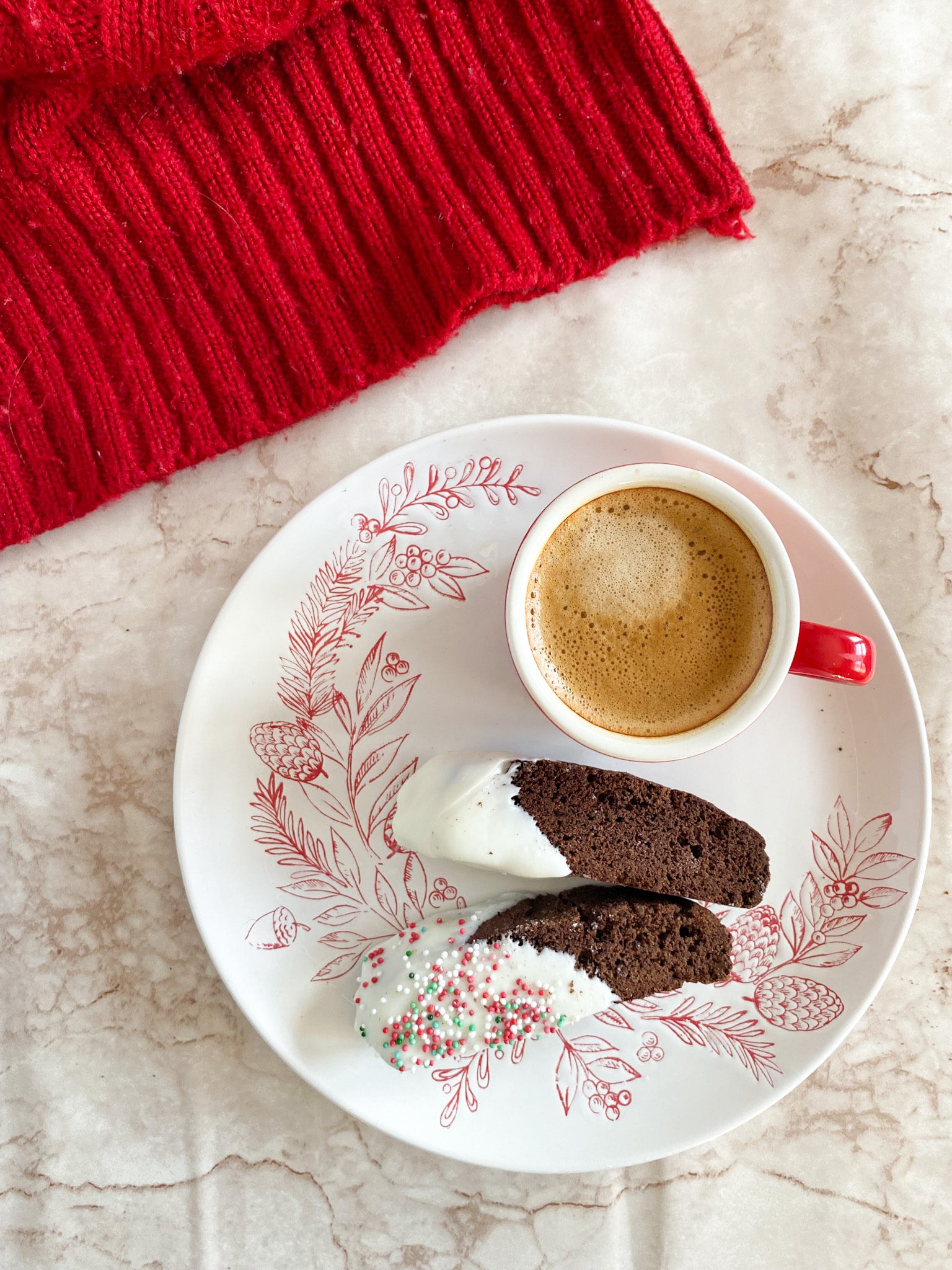 chocolate gingerbread biscotti dipped in white chocolate sit on a white plate with red holiday decor