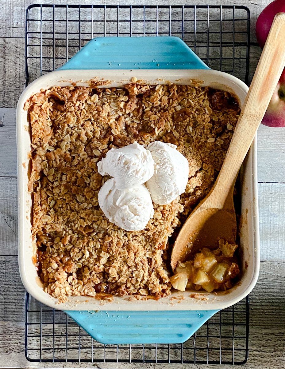 A teal colored baking pan full of apple crisp topped with ice cream.