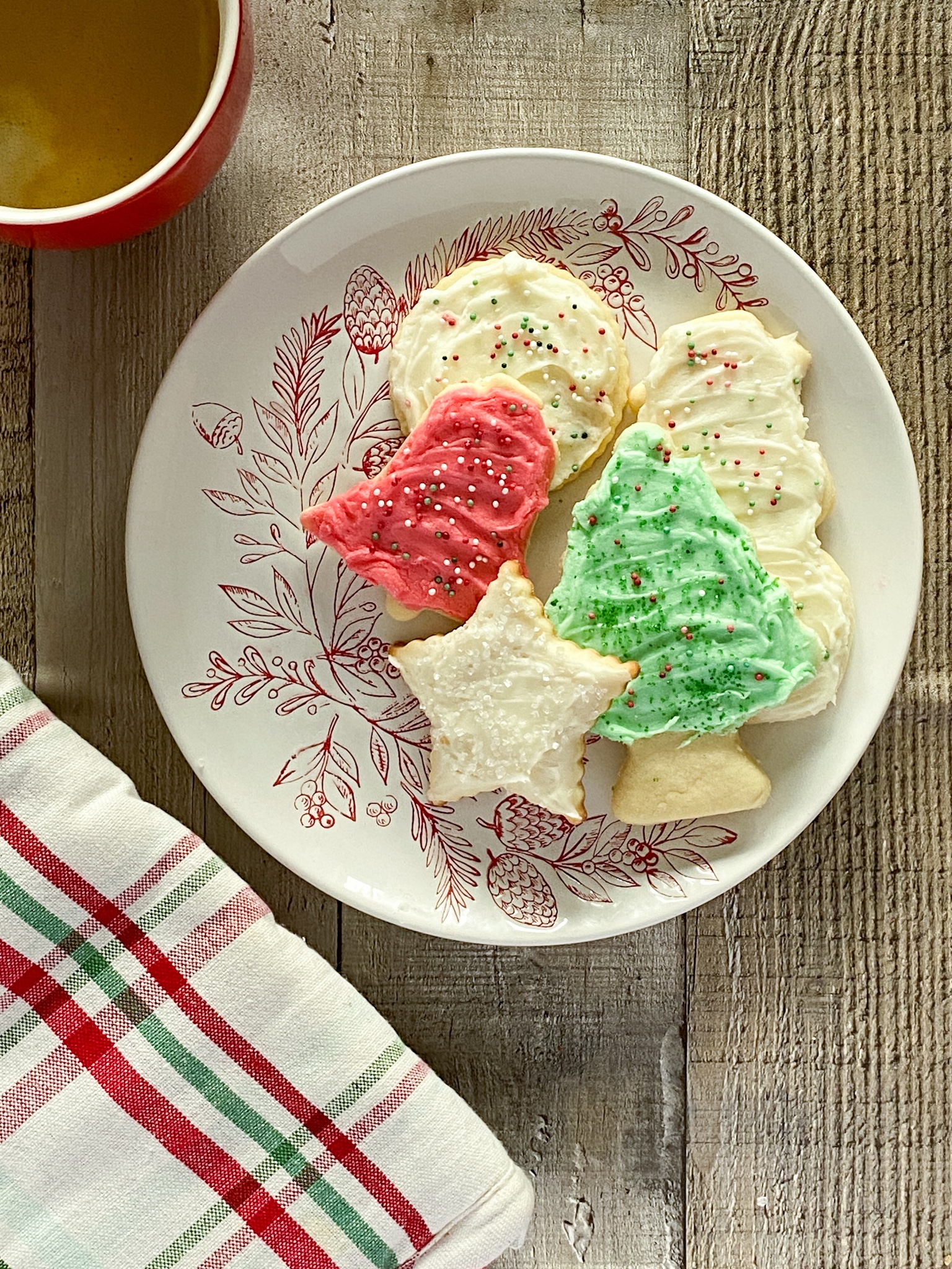 Sugar cookies cut in holiday shapes and decorated with colored frosting on a Christmas plate.