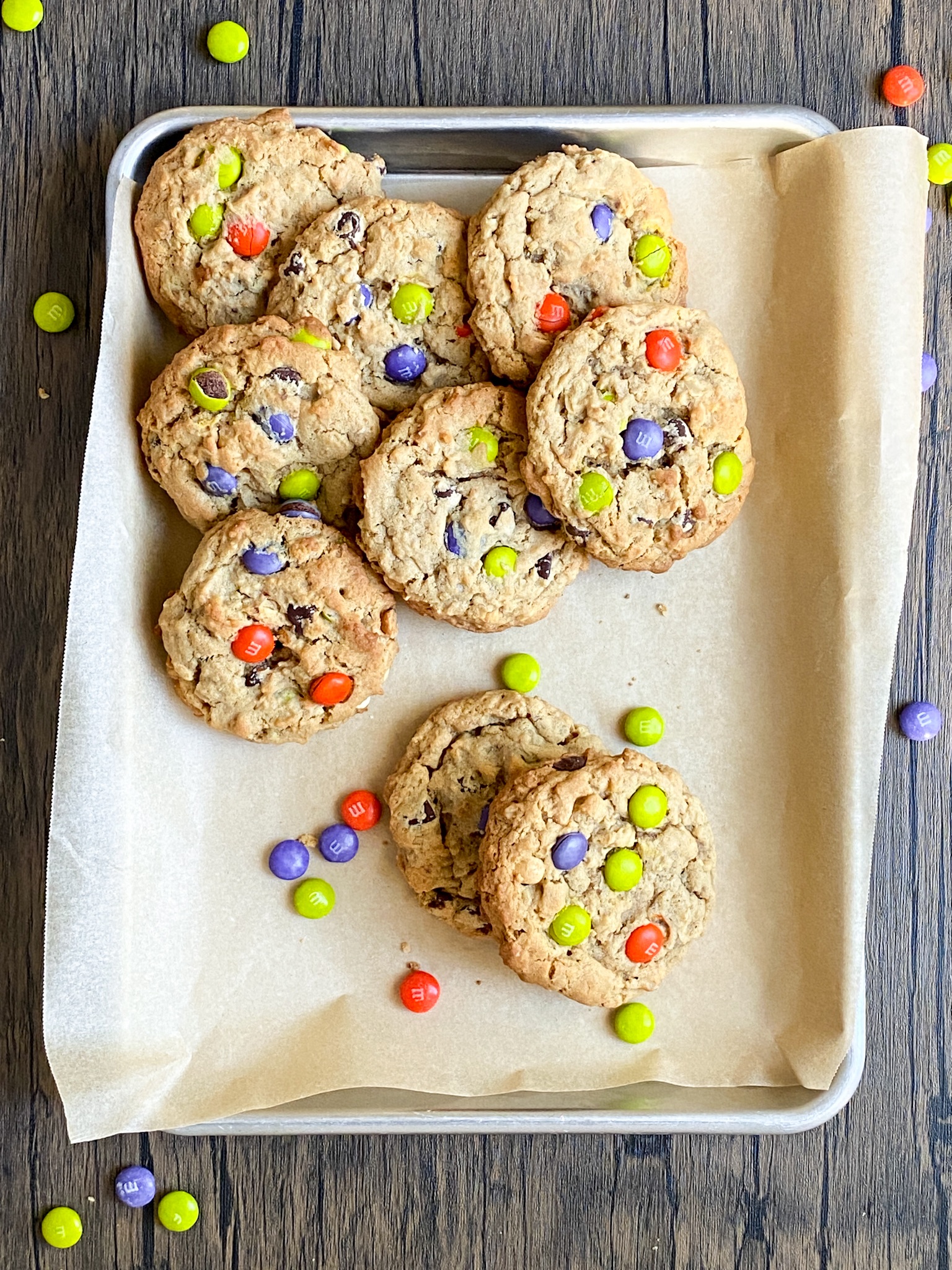 a pile of monster cookies with brightly colored candy pieces sit on parchment paper.