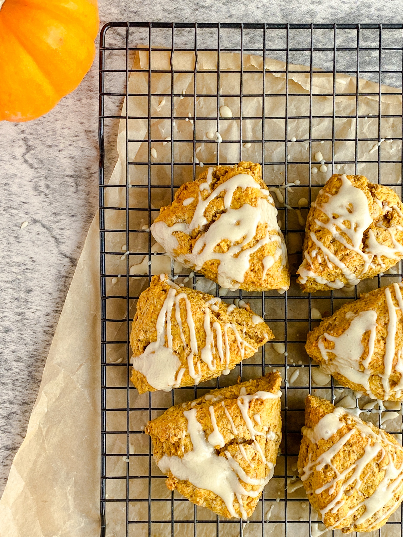 pumpkin scones drizzled with glaze sit on a cooling rack on a marbled surface.