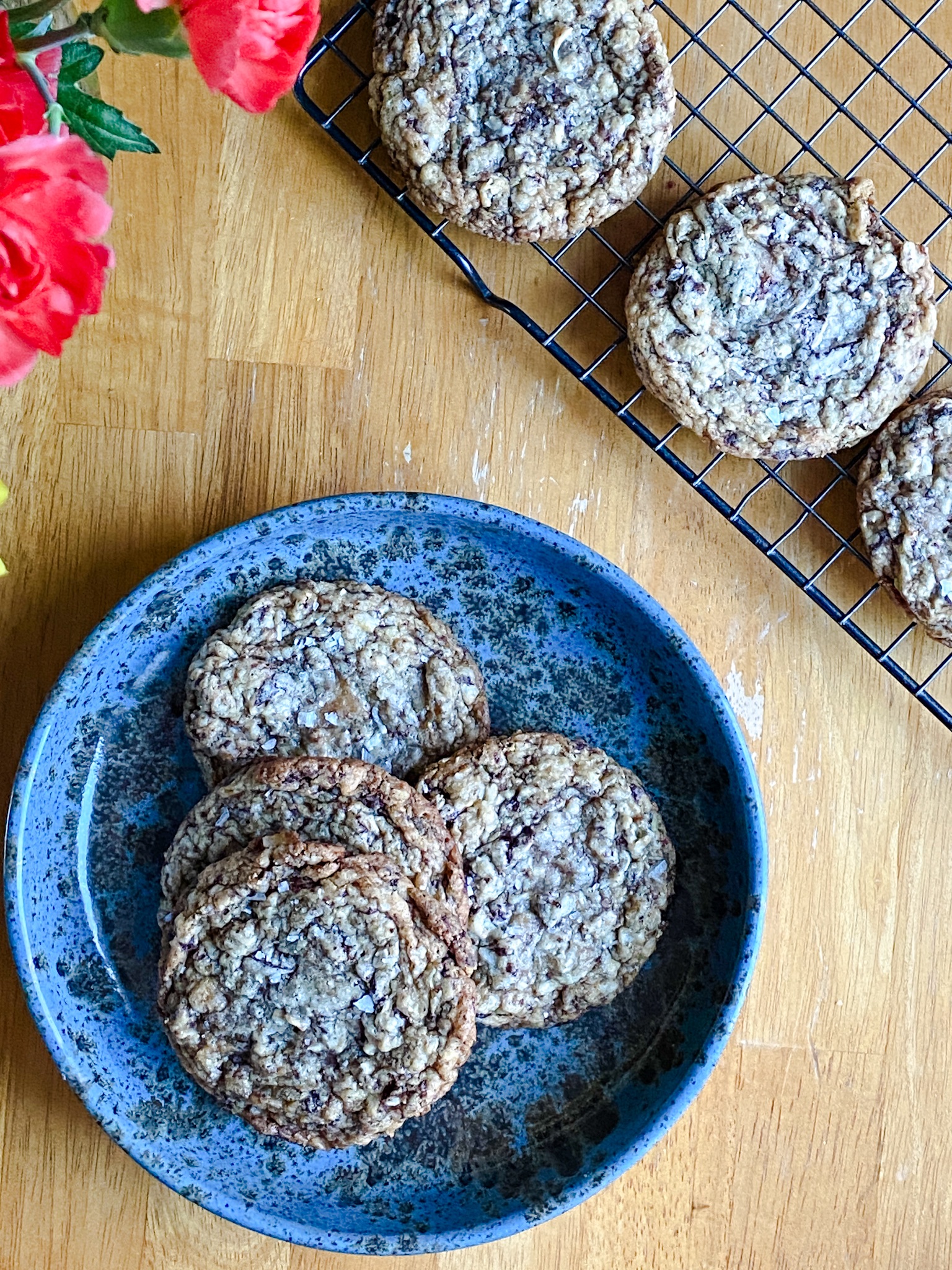 chocolate chip cookies on a blue plate, with more on a cooling rack beside it.