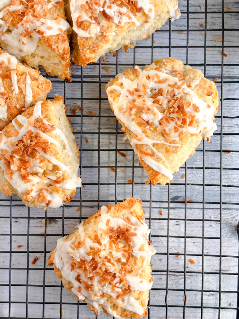 Flaky coconut scones sit on a cooling rack. They're drizzled with icing and sprinkled with coconut.