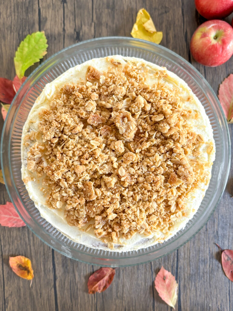 A top shot of a layer cake covered in oatmeal crisp topping. It sits on a cake stand on a wood surfa