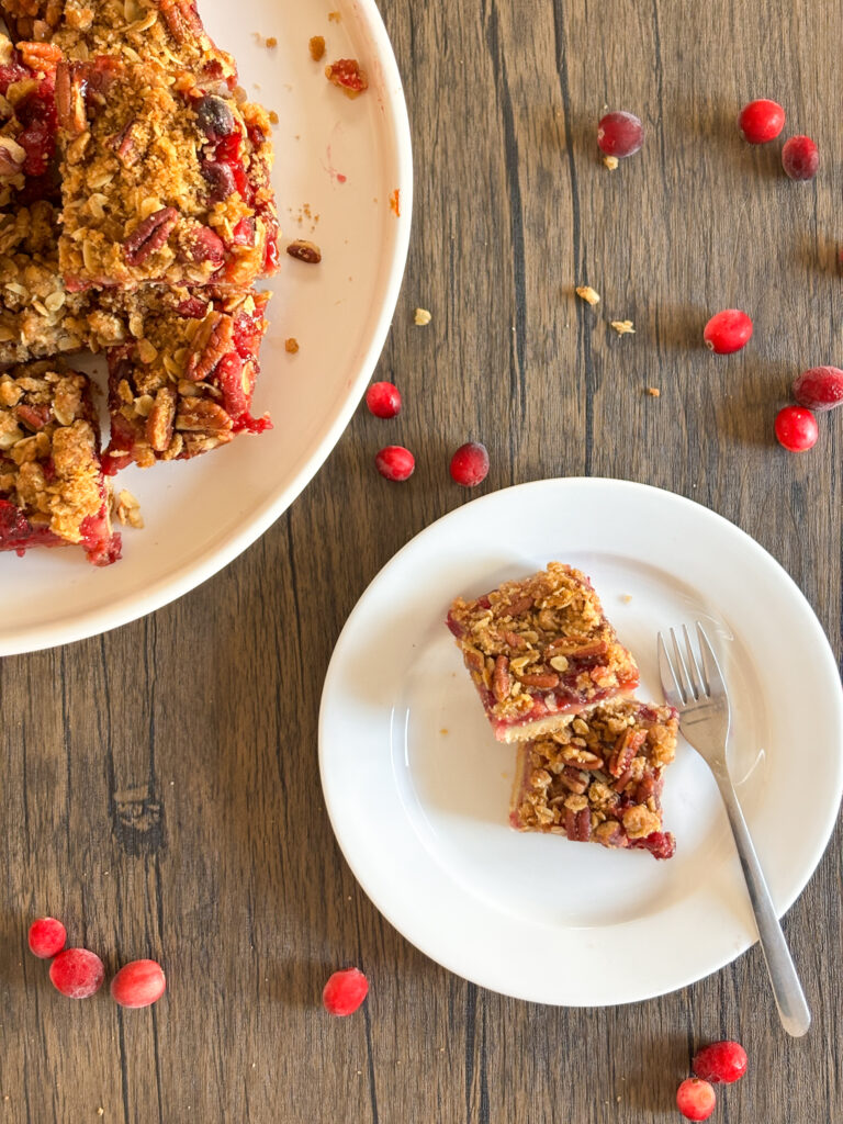 cranberry crumble bars sit on a plate with a fork next to them on a wooden surface
